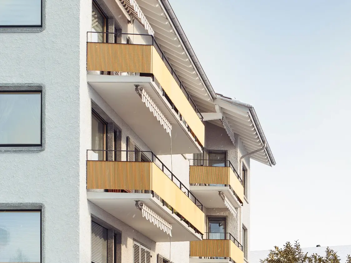 Seitenansicht mit weiss verputzter Fassade und gelben Balkongeländern