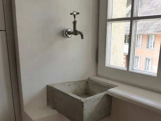 Eckwaschbecken aus Stein mit historisch anmutendem Wasserhahn aus der Wand