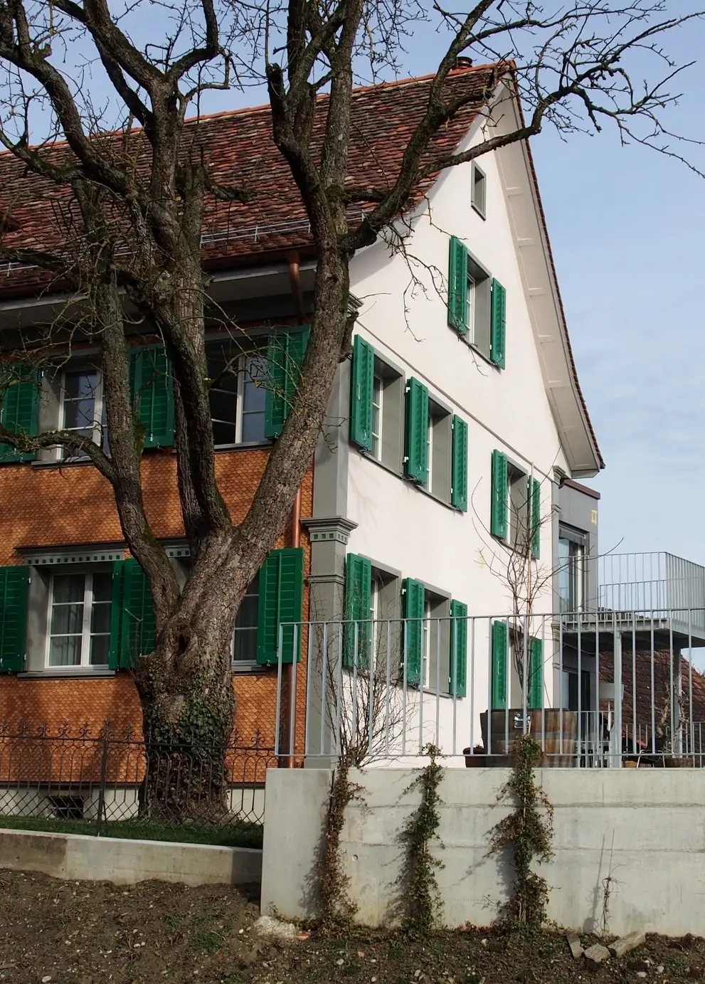 Gebäudeseite mit Baumstämmen vor dem Haus