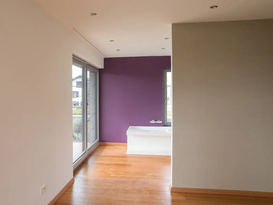 Vue sur un mur intérieur violet foncé, devant lequel se trouvent une baignoire blanche ainsi qu'une cloison crépie en blanc