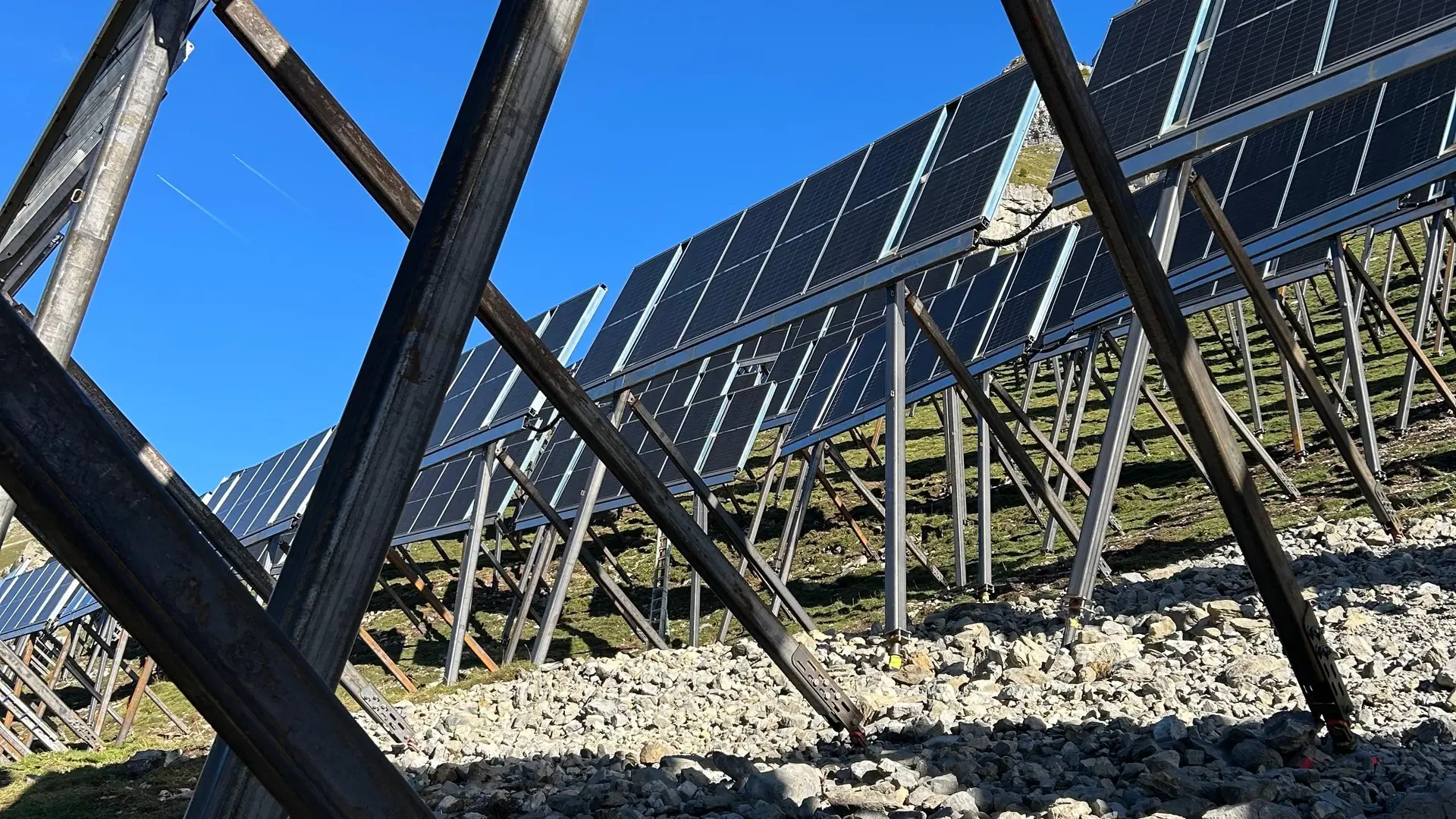 Deux montants métalliques sont ancrés dans le sol gravelé, derrière lesquels on aperçoit de nombreux modules photovoltaïques déjà installés.