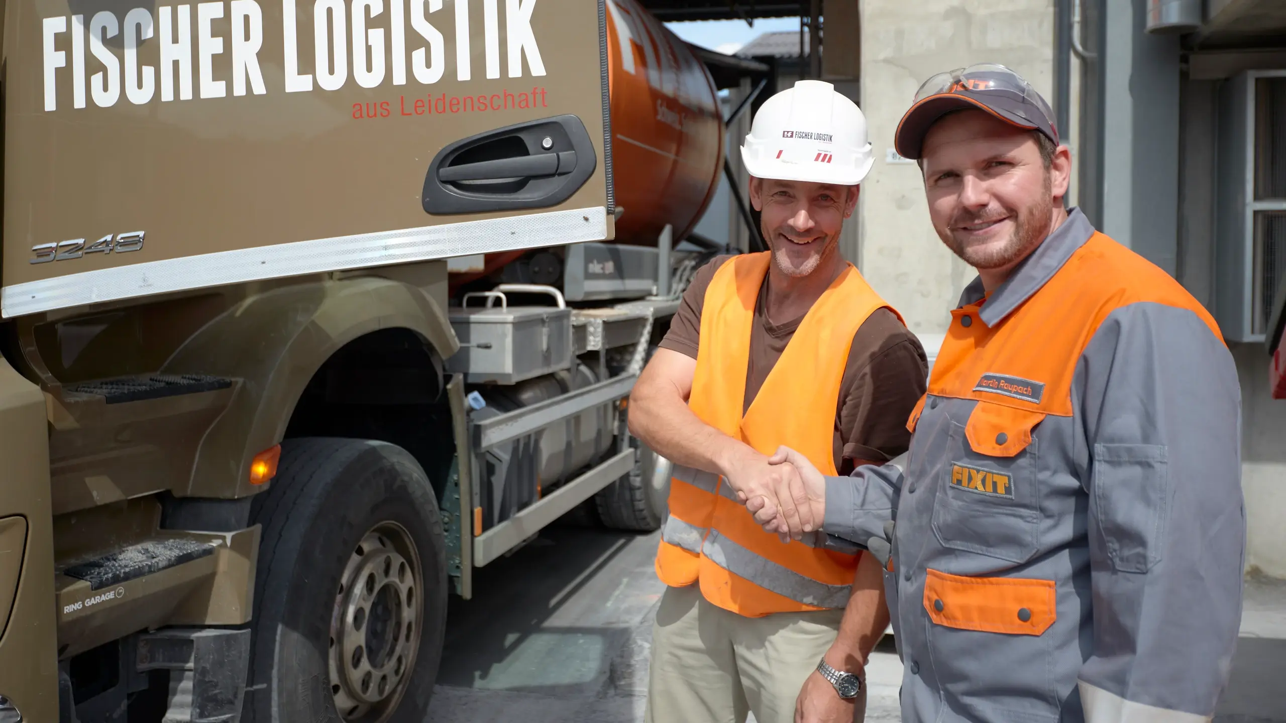 Due dipendenti Fixit si stringono la mano davanti a un camion della Fischer Logistik