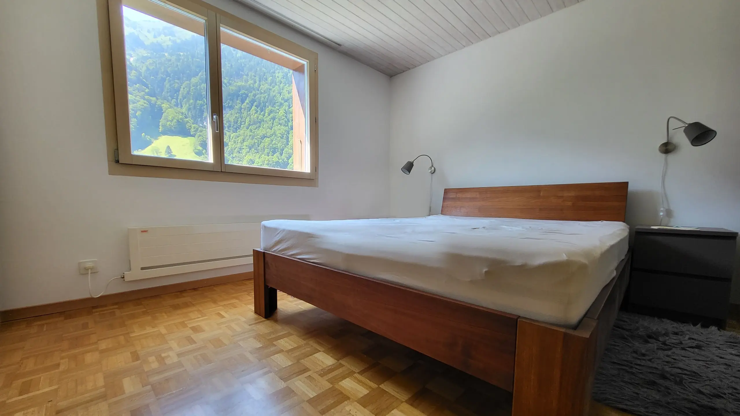 Chambre à coucher avec parquet à baguettes, grand lit en bois et murs intérieurs blancs rénovés avec Fixit 252
