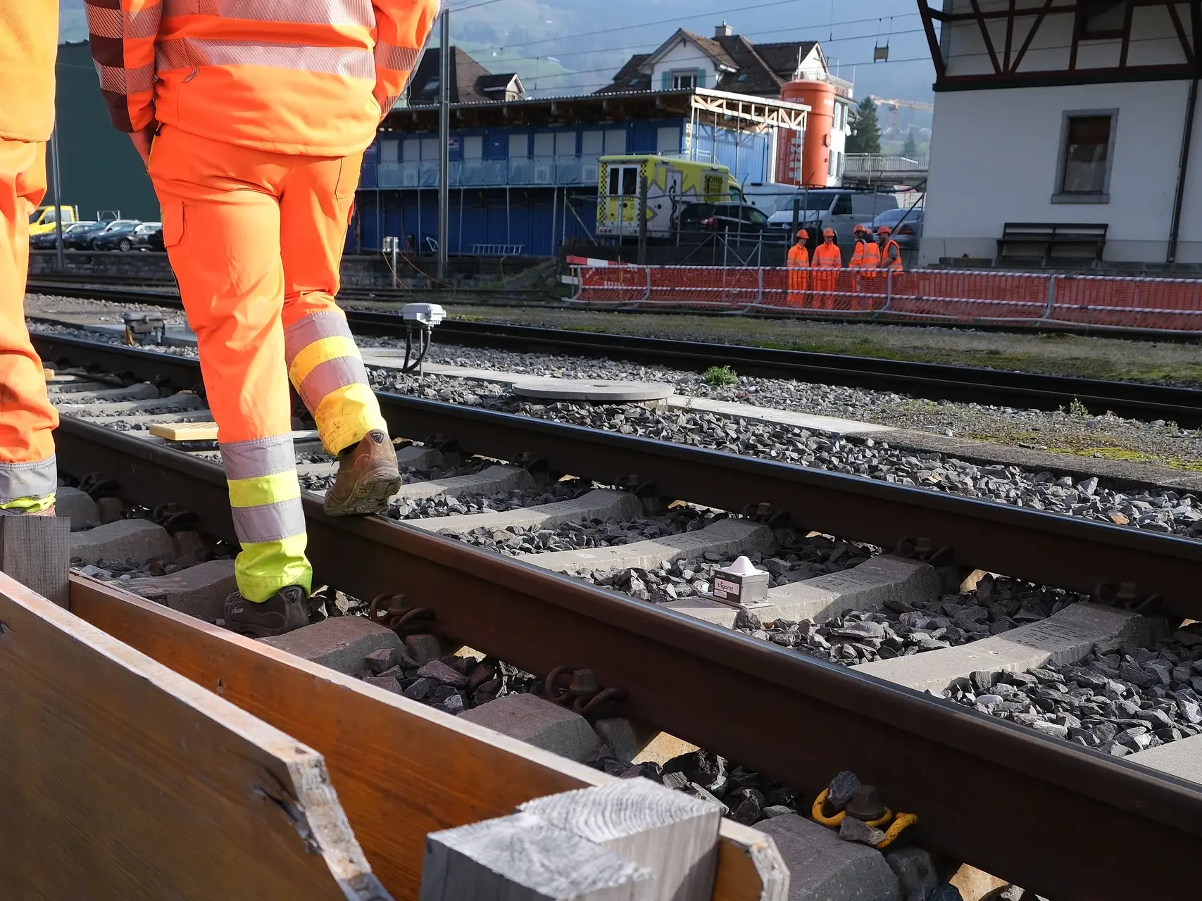Zwei Bauarbeiter in orangener Arbeitskleidung laufen am Gleisbett mit dem Sichtschacht für die Verfüllung mit Fixit POR vorbei