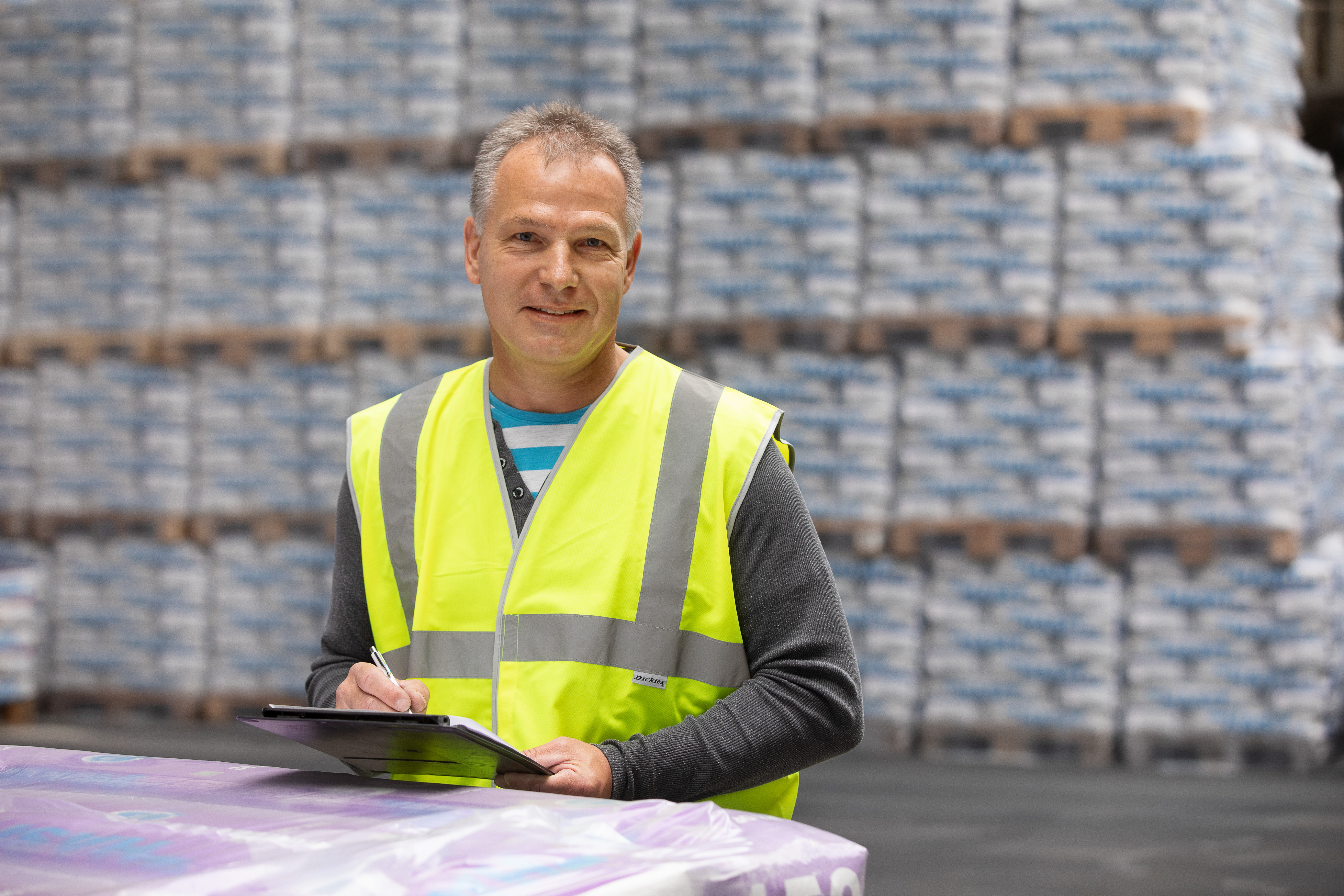 Werksmitarbeiter im Vordergrund eines Lagers mit einer Menge Paletten, die mit Produktsäcken beladen sind