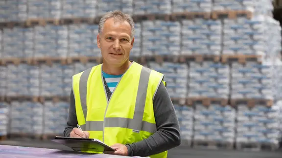 Werksmitarbeiter im Vordergrund eines Lagers mit einer Menge Paletten, die mit Produktsäcken beladen sind