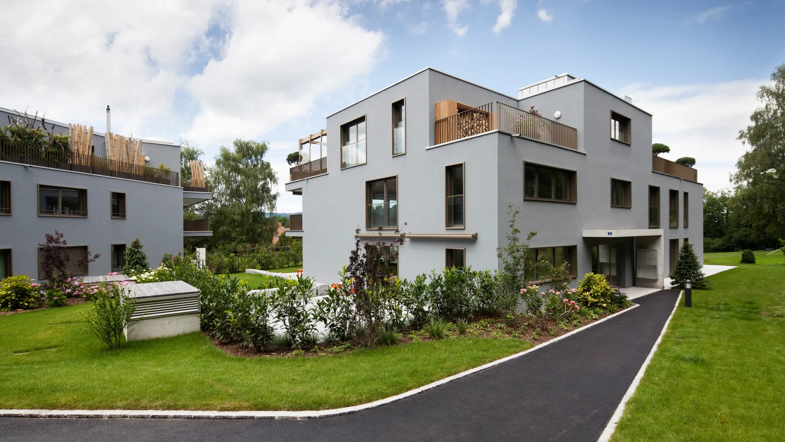 Modernes, kubisches Mehrfamilienhaus mit grünem Garten und weissem Aussenputz