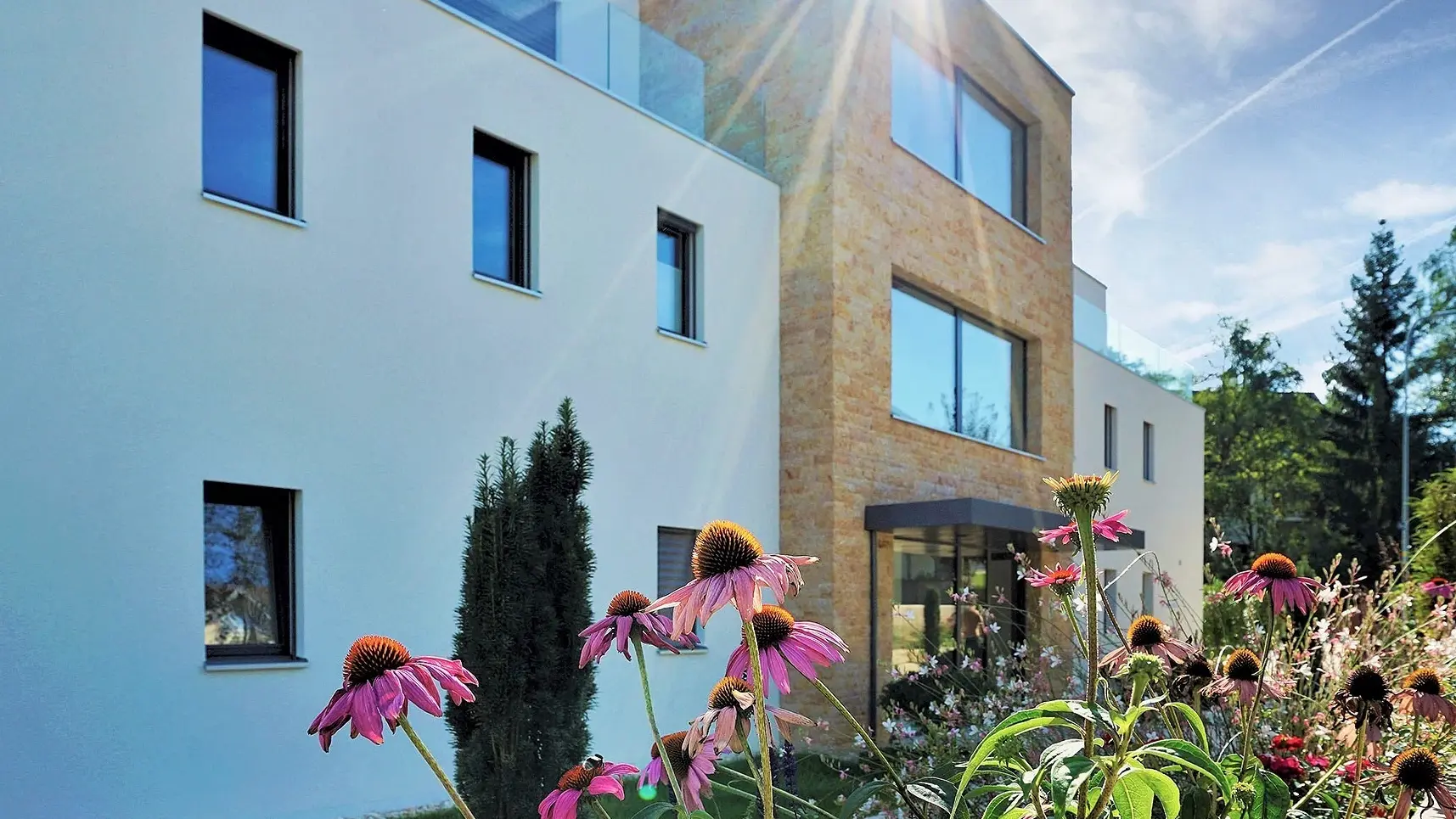 Rosa Blumen vor einer weiss verputzten Aussenfassade mit Natursteinelementen