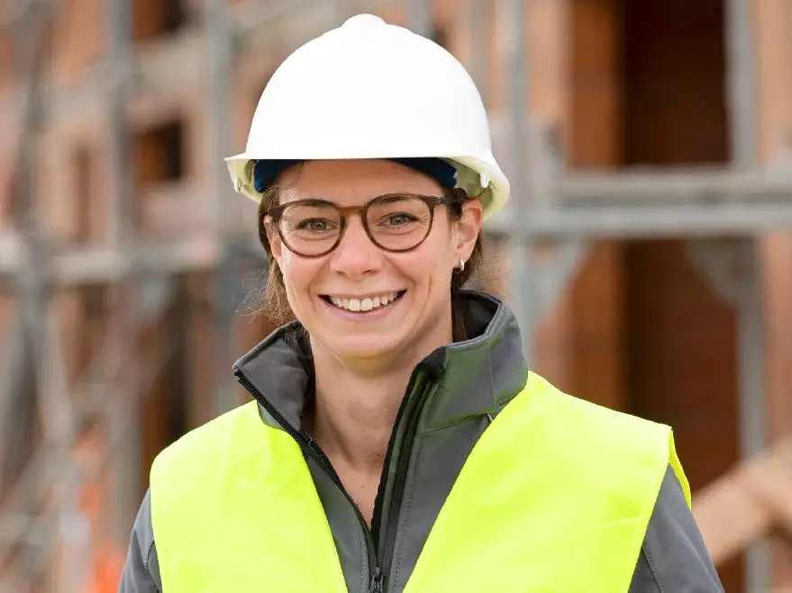 Donna con occhiali, elmetto da cantiere bianco e giubbotto di sicurezza giallo brillante per un edificio in fase di costruzione