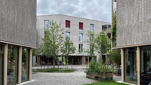 Links und rechts zweifarbige Fassade mit Fixit Produkten und mittig im Hintergrund ein komplettes Gebäude der Huebergass Genossenschaft