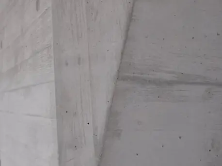 Gros plan sur une surface en béton apparent présentant des angles particuliers et des empreintes horizontales