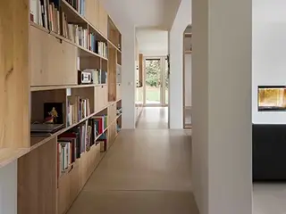 Salon moderne avec une grande étagère en bois pour les livres sur la gauche, un canapé noir, des murs et un plafond en plâtre.