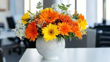 Bouquet mixte sans roses avec fleurs oranges, jaunes et blanches dans un vase en céramique blanche
