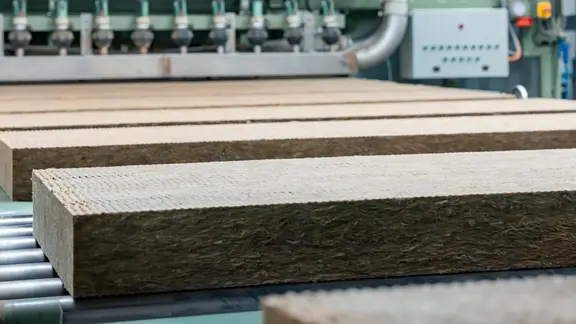 Des panneaux isolants en laine de pierre découpés passent sur un tapis roulant dans la halle de production de Flumroc
