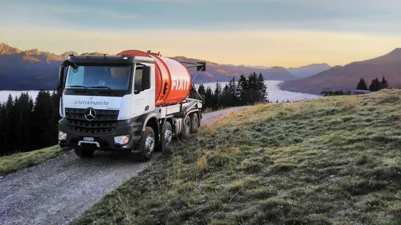 Un camion avec un silo de Fixit roule sur une route de montagne étroite. En arrière-plan, on voit un panorama au lever du soleil.