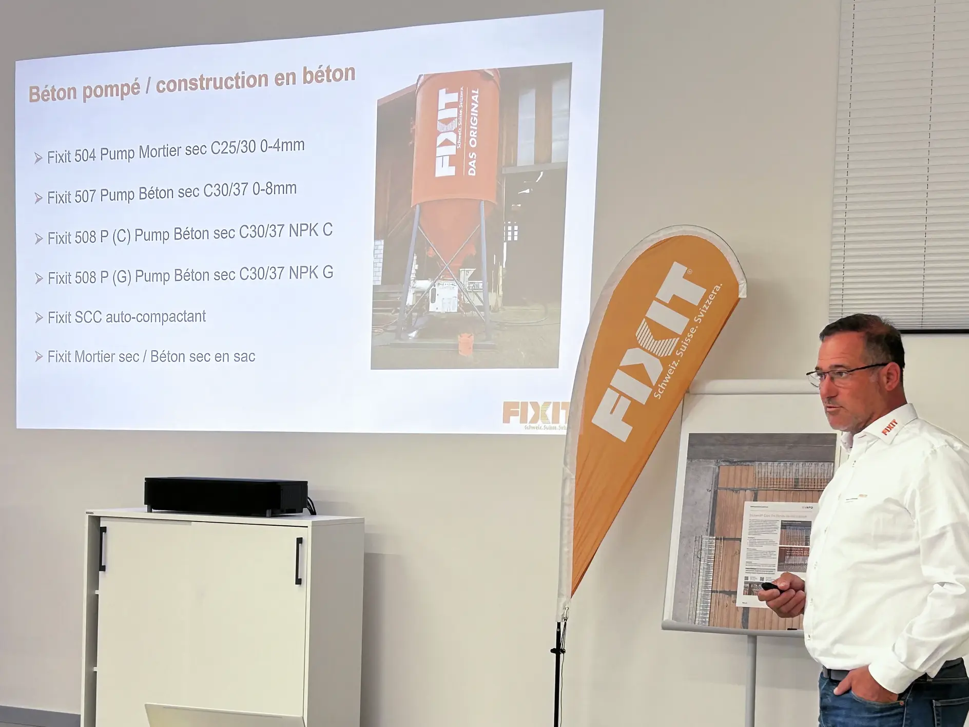 Nelson Carvalho présente une diapositive sur les pompes à béton Fixit et les produits en béton Fixit avec une photo d'un silo Fixit.