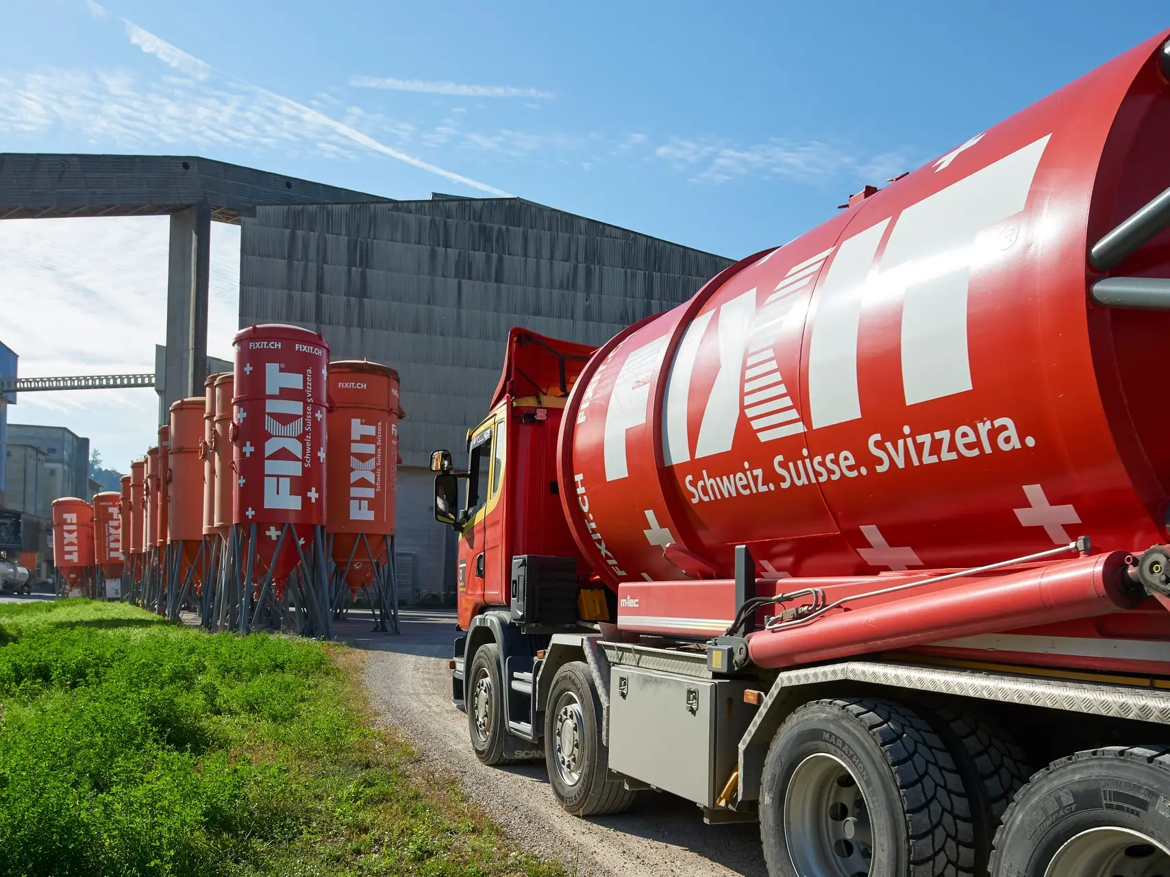 Un silo Fixit sur un camion au premier plan, et à l'arrière-plan d'autres silos Fixit ainsi que l'usine de production de Holderbank