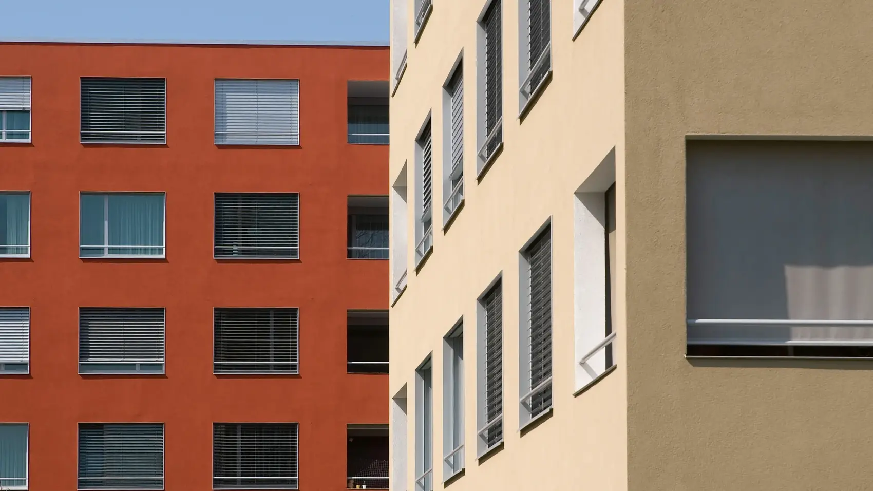 Bâtiment de plusieurs étages de couleur rouge rouille à l'arrière-plan et bâtiment beige en coin à droite au premier plan