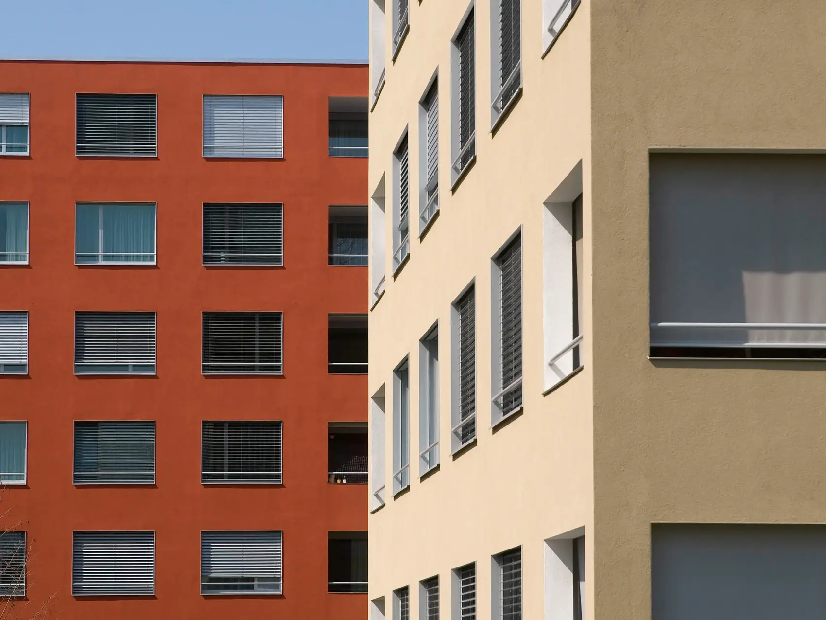 Bâtiment rouge rouille à plusieurs étages à l'arrière-plan et, à droite, un coin de bâtiment jaune clair au premier plan