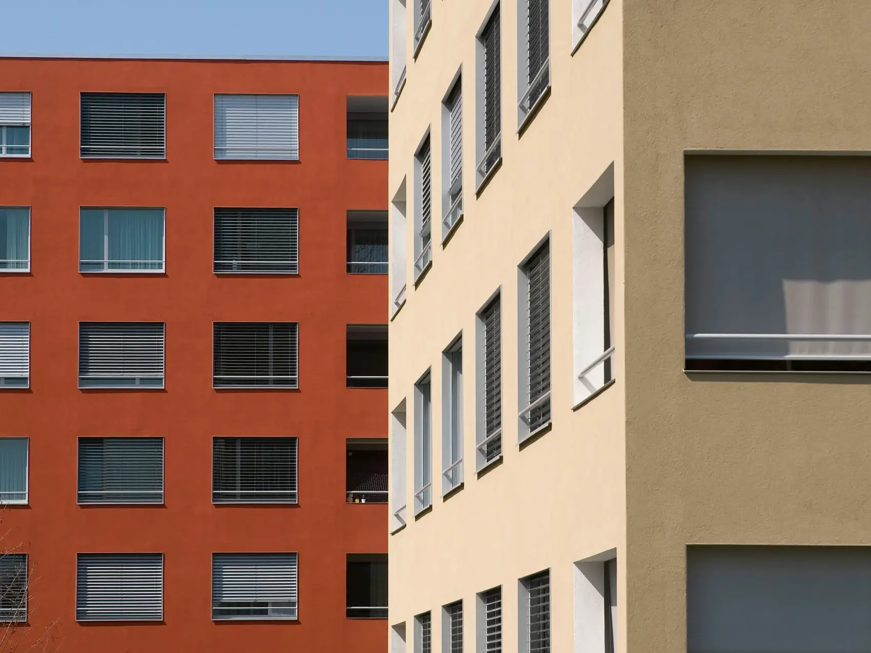Bâtiment de plusieurs étages rouge rouille à l'arrière-plan et bâtiment beige en coin à droite au premier plan