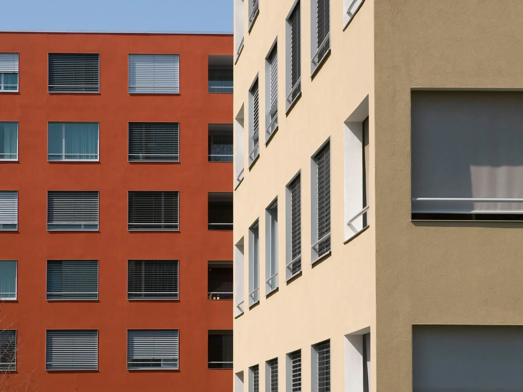 Bâtiment de plusieurs étages rouge rouille à l'arrière-plan et bâtiment beige en coin à droite au premier plan
