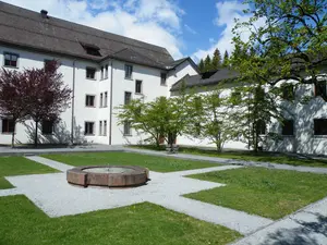 Symmetrischer Rasen mit Steinbrunnen in der Mitte im Innenhof des Klosters Pfäfers im Hintergrund