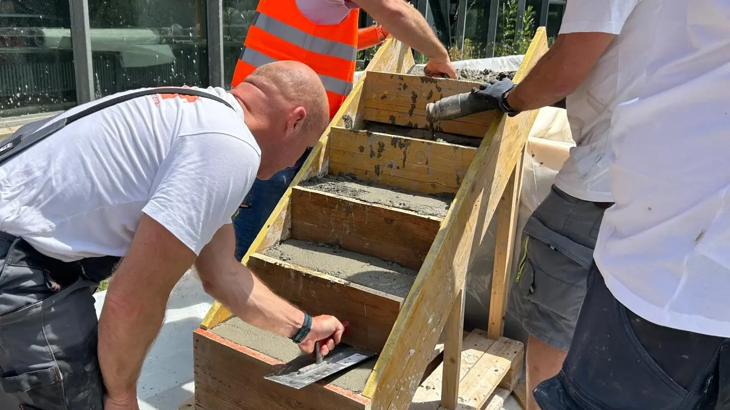 Drei Mitarbeitenden verspachteln eine mit Frischbeton gefüllte Treppen-Verschalung aus Holz