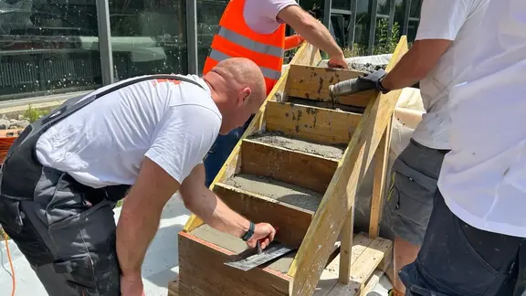 Drei Mitarbeitenden verspachteln eine mit Frischbeton gefüllte Treppen-Verschalung aus Holz