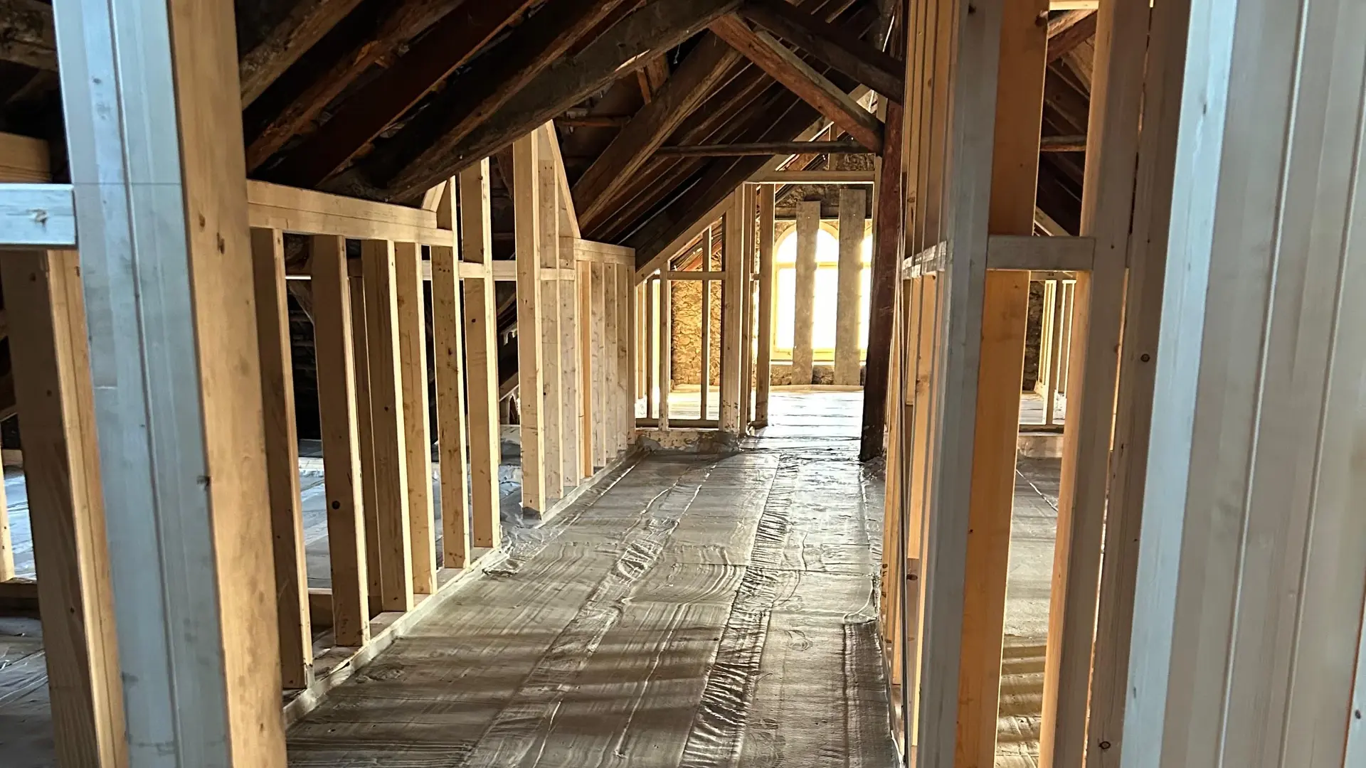 Dachgeschoss mit Holzbalken-Ständerwerk und einem aufgefüllten Boden, Sonne scheint durch ein Fenster und wirft Schatten