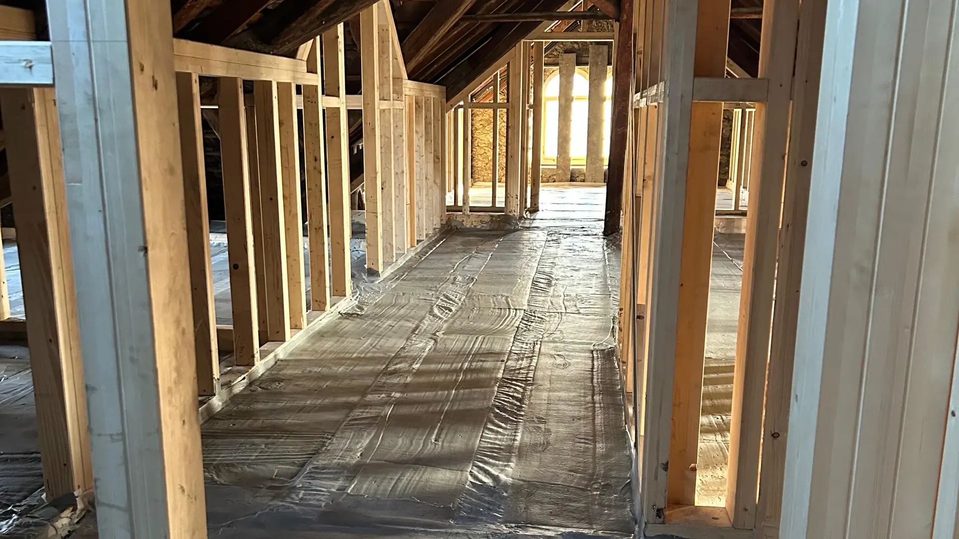 Dachgeschoss mit Holzbalken-Ständerwerk und einem aufgefüllten Boden, Sonne scheint durch ein Fenster und wirft Schatten