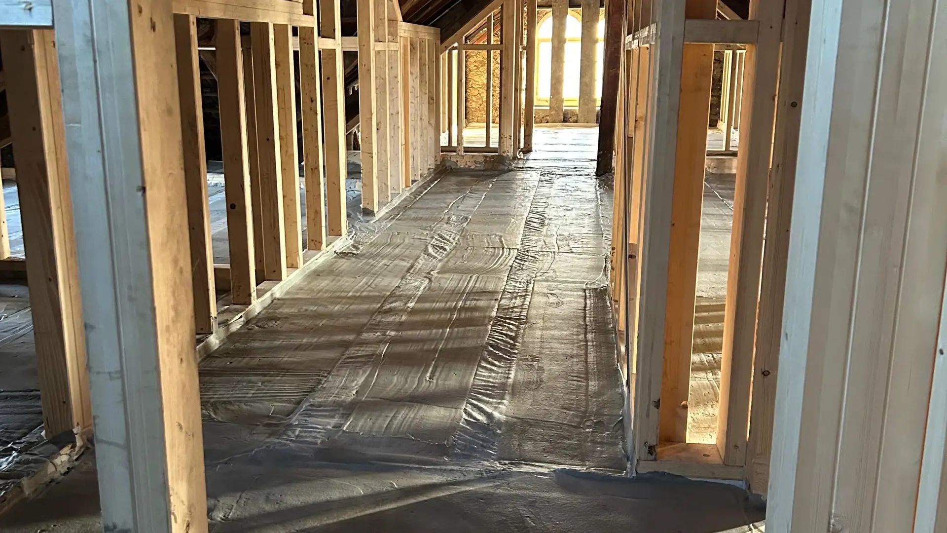 Dachgeschoss mit Holzbalken-Ständerwerk und einem aufgefüllten Boden, Sonne scheint durch ein Fenster und wirft Schatten