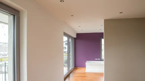 Innenraum mit weiss verputzten Wänden sowie einer auberginefarbenen Wand im Hintergrund der Badewanne
