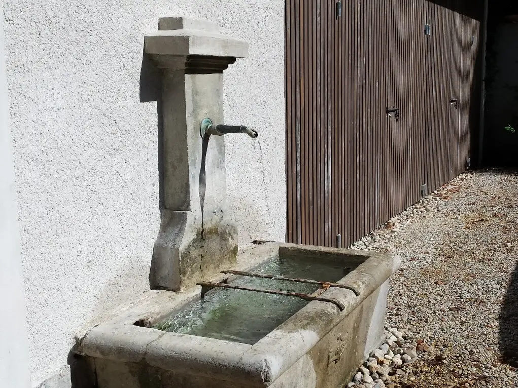 Steinbrunnen, der in die verputzte Wand eingelassen ist mit einem Steintrog darunter voll mit Wasser