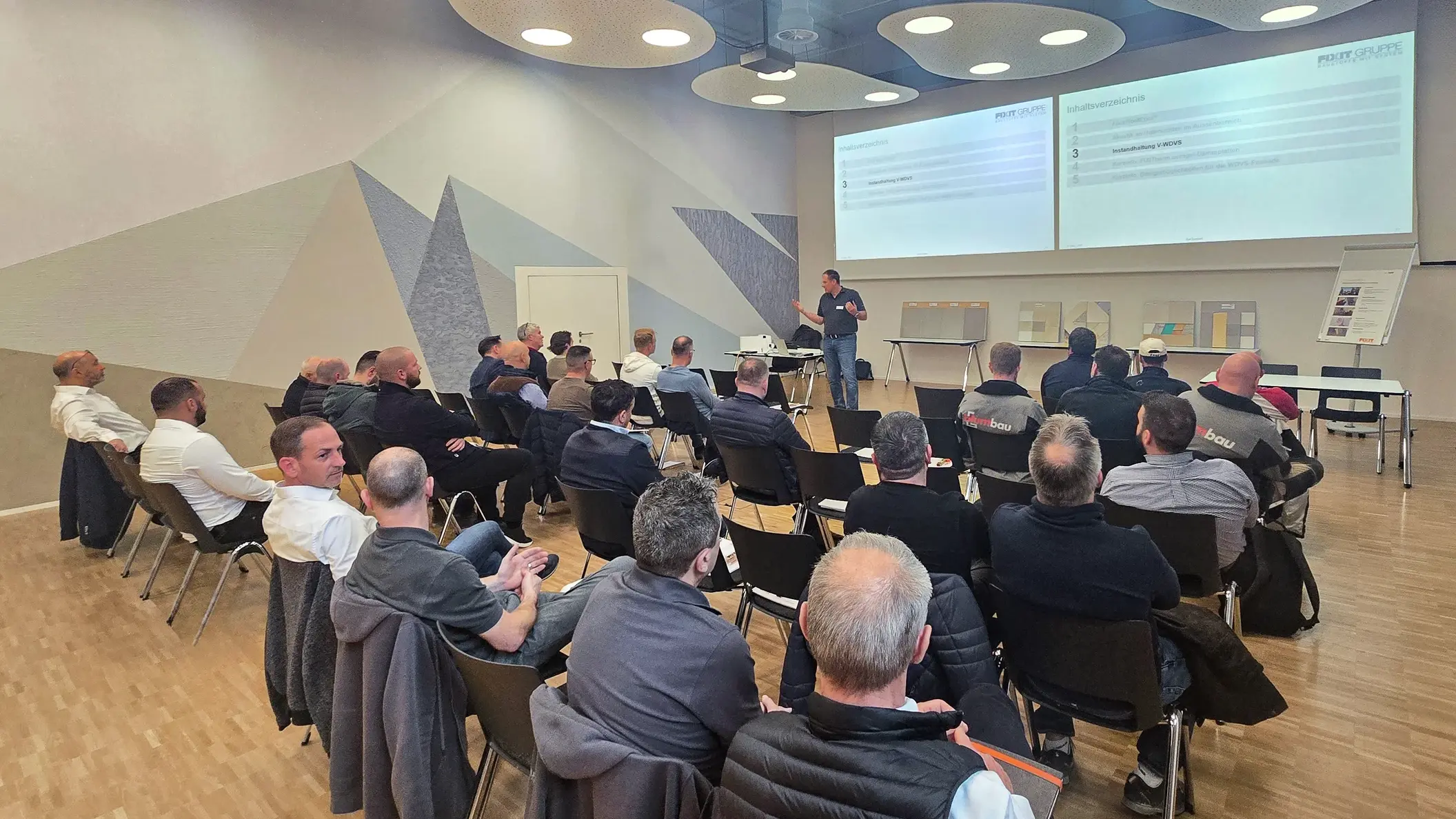 Ansicht auf alle Teilnehmenden, die in Reihen vor der Präsentation von Ralf Bannwitz sitzen