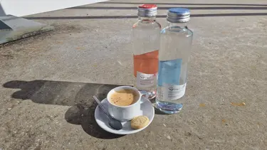 Une petite tasse de café avec un biscuit et deux bouteilles d'eau au soleil