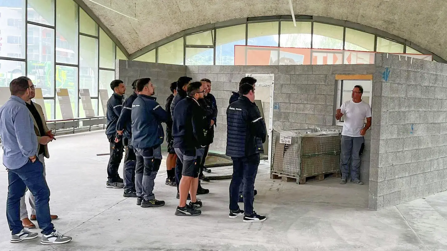 Le groupe des collaborateurs du magasin Getaz-Miauton SA se tient à gauche et un technicien d'application Fixit montre les points problématiques sur un mur d'échantillons.