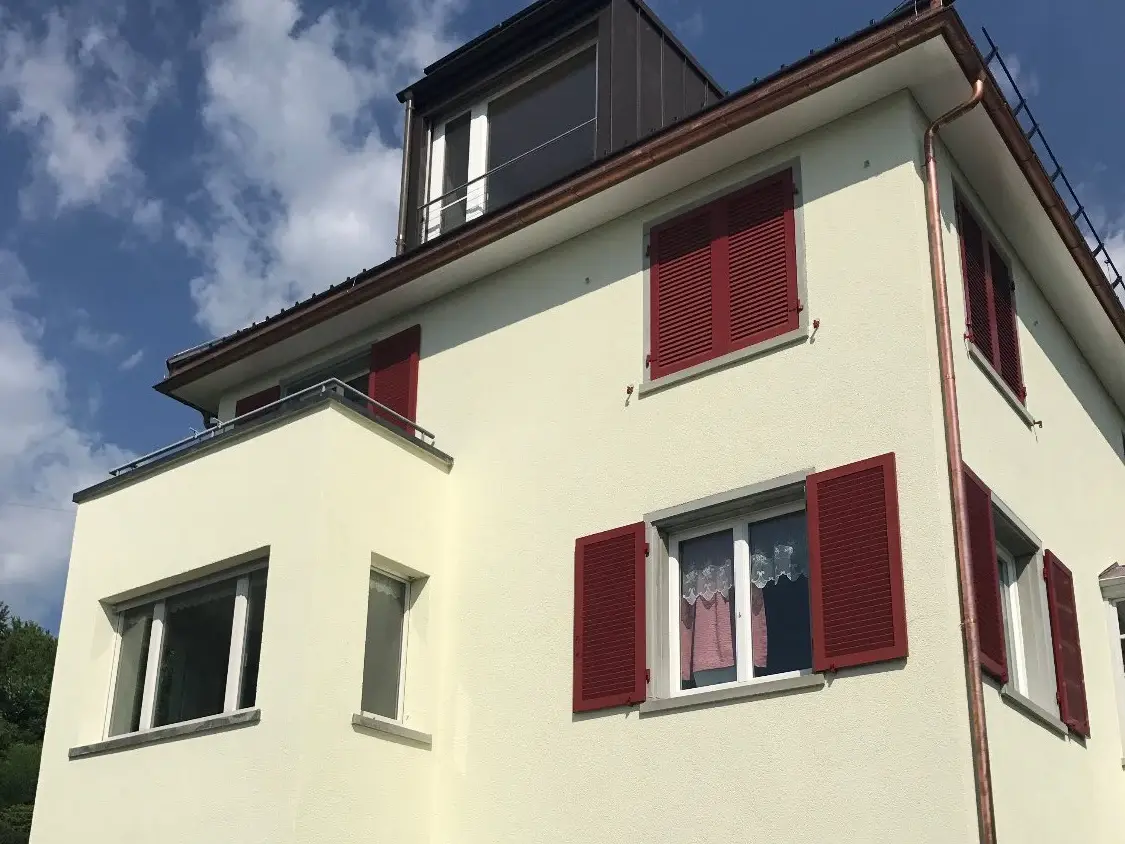 Hellgelb verputztes Gebäude mit roten Fensterläden