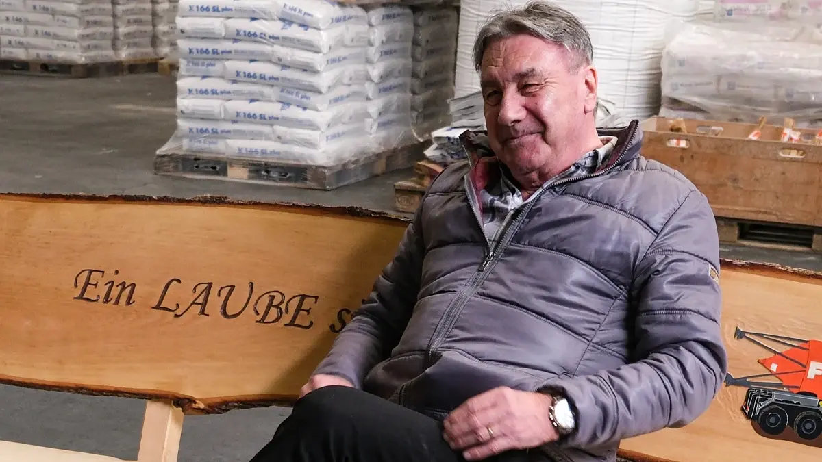 Aussendienstmitarbeiter Markus Laube auf seinem Geschenk zur Pension: einer Baumstamm-Bank für den Garten