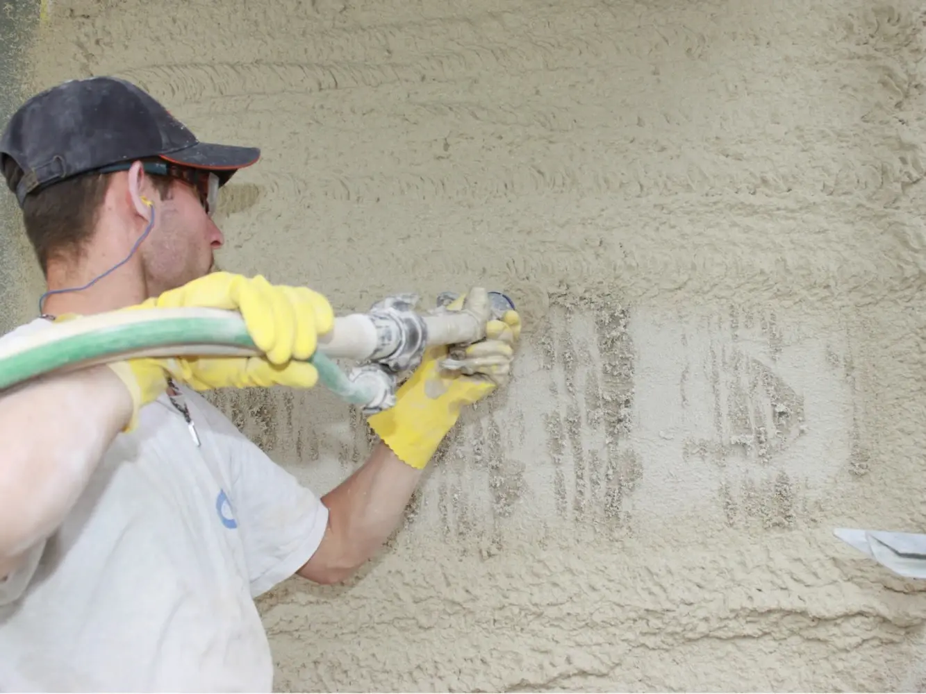 Ein Verarbeiter mit grauer Kappe und gelben Handschuhen spritzt den Fixit 222 Dämmputz an die Wand