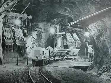 Historische Schwarz-Weiss Fotografie eines Bergwerks mit Lorenzug und Maschinenvorrichtungen
