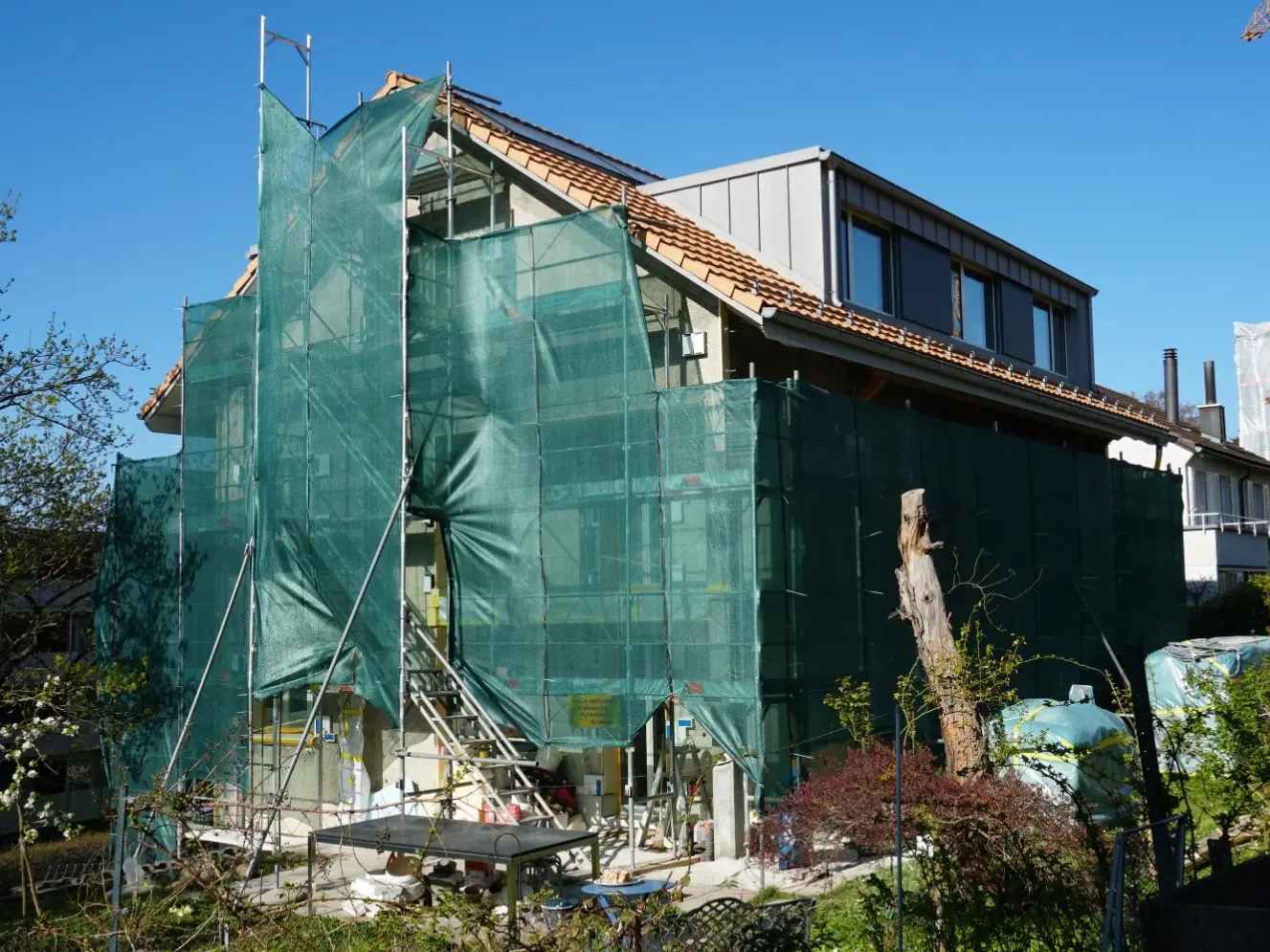 La maison individuelle échafaudée, avec un filet de protection de façade vert, sous le soleil