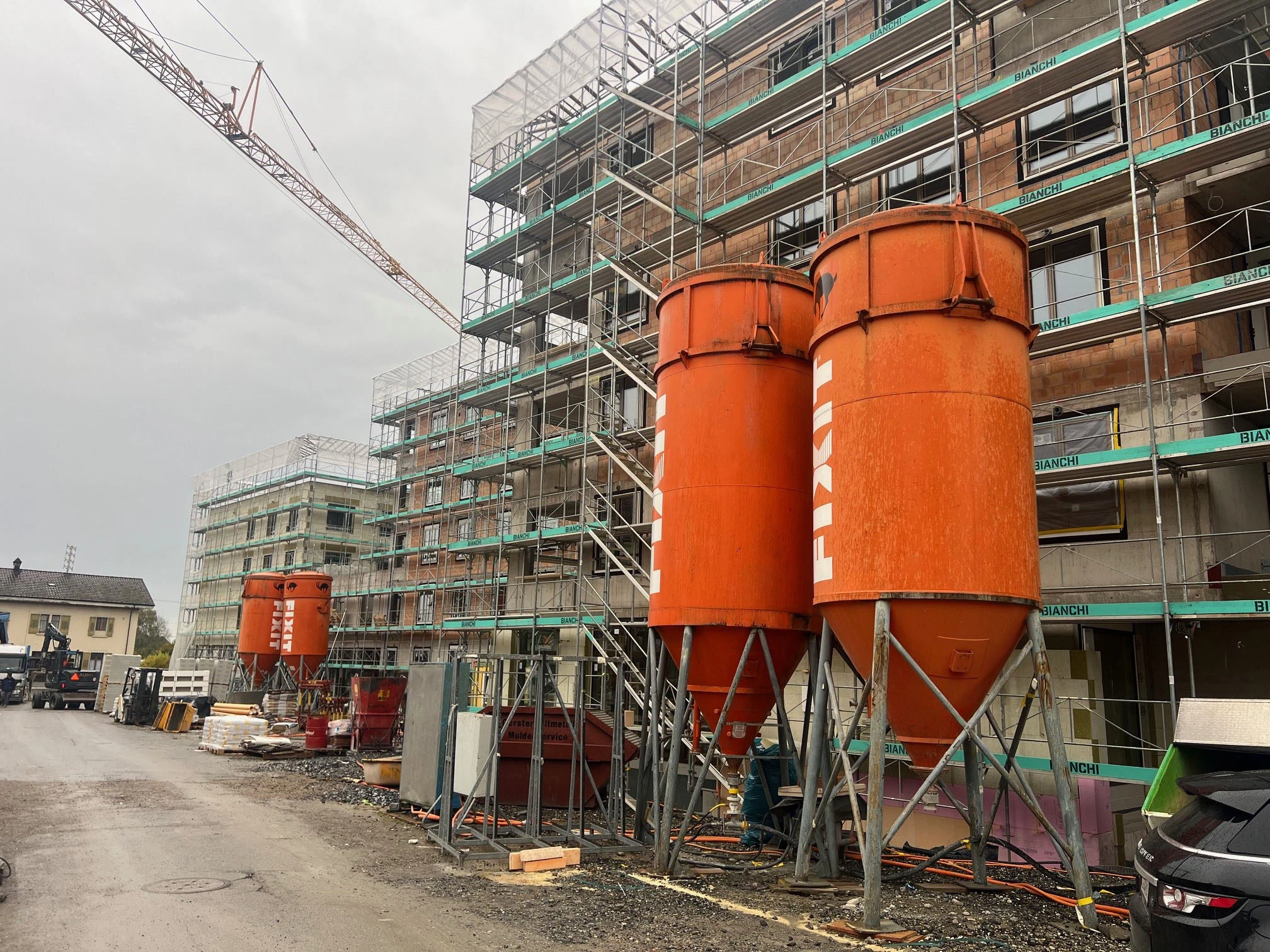 [Translate to French (CH):] Zwei orangene Fixit Silos vor dem eingerüsteten Gebäude Perron Vert in Egnach