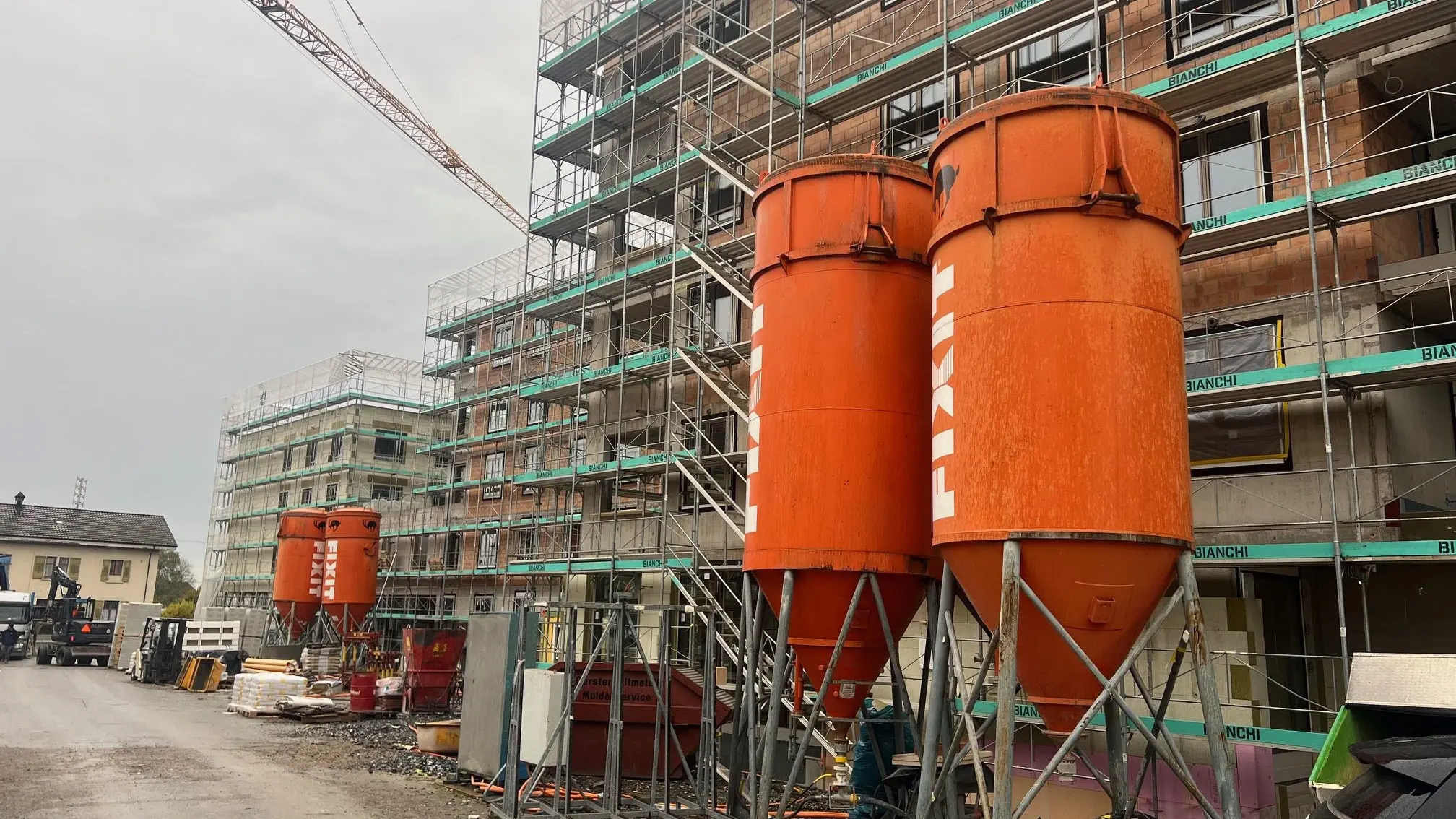 Deux silos Fixit orange devant le bâtiment Perron Vert à Egnach, entouré d'échafaudages.