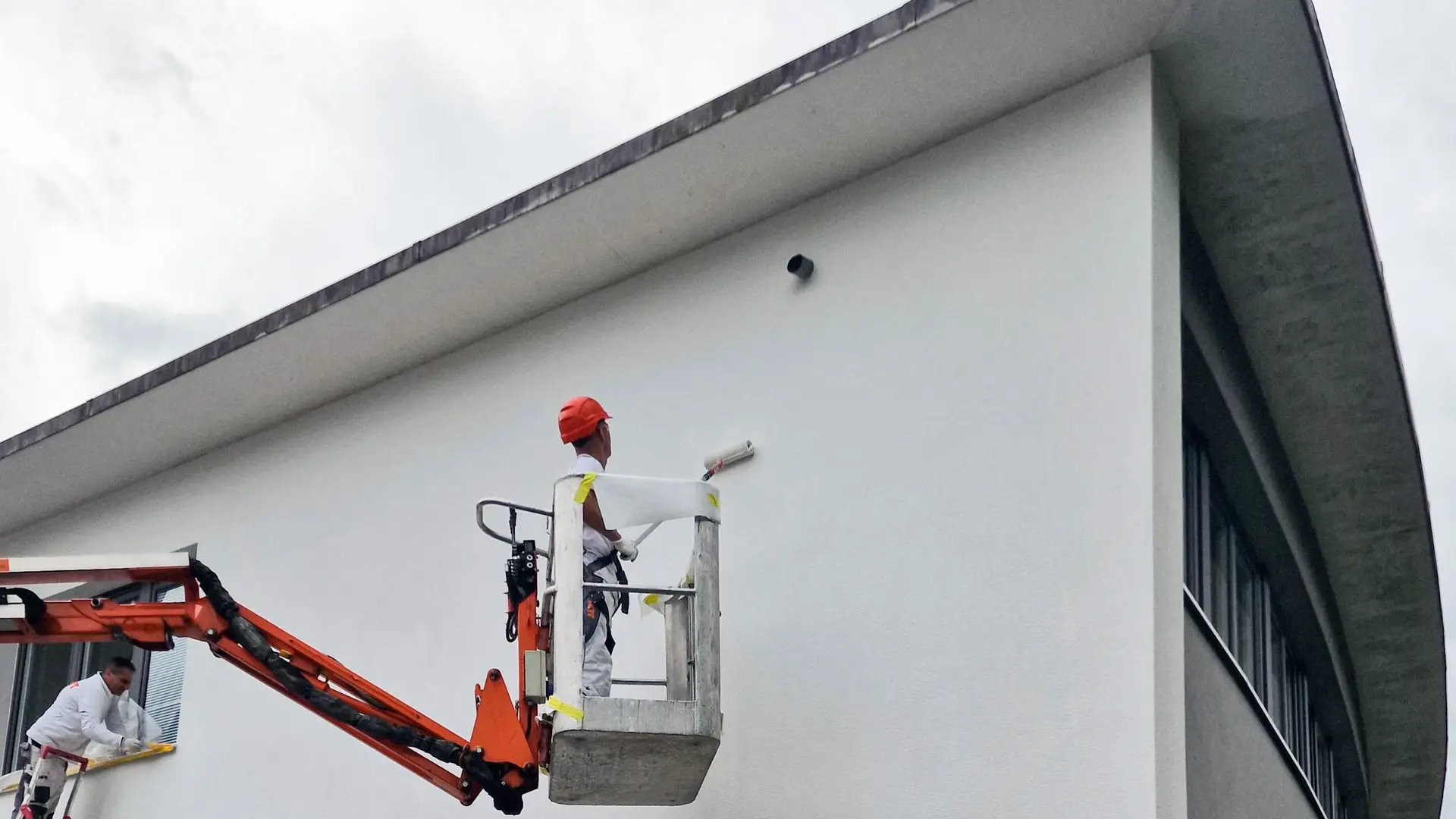 Maik Schneider auf Hebebühne streicht die Nordfassade des Verwaltungsgebäudes in Holderbank AG mit der Farbrolle