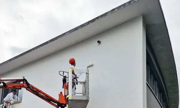 Maik Schneider auf Hebebühne streicht die Nordfassade des Verwaltungsgebäudes in Holderbank AG mit der Farbrolle