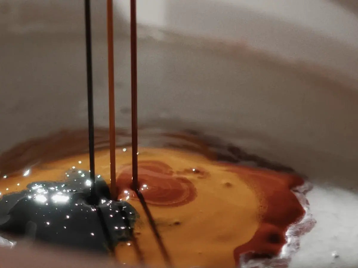 Vue détaillée d'un seau ouvert contenant de la peinture blanche, à laquelle sont ajoutés trois jets de peinture orange, rouge et noire