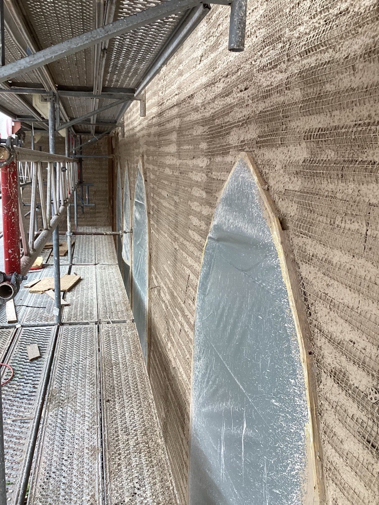 : Das Gebäude während der Bauphase – eingerüstet von außen, mit Detailaufnahmen der Dämmputzverarbeitung an den Fensterbereichen.