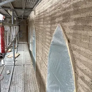 : Das Gebäude während der Bauphase – eingerüstet von außen, mit Detailaufnahmen der Dämmputzverarbeitung an den Fensterbereichen.