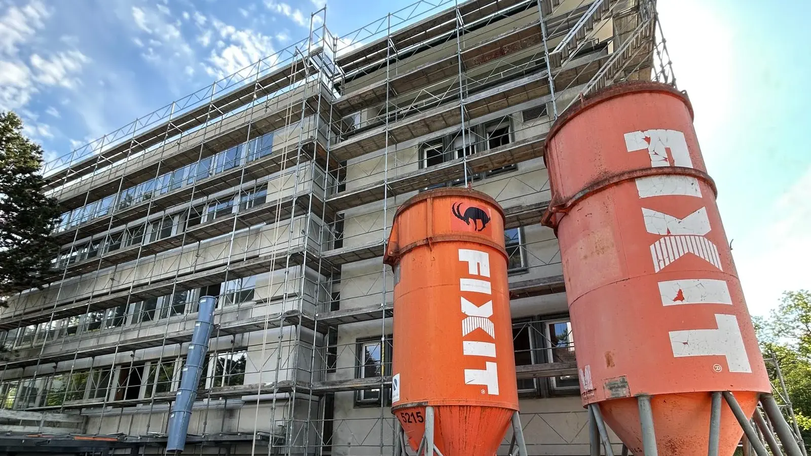 Zwei orangene Fixit Silos im Vordergrund vor einem mehrstöckigen, eingerüsteten Gebäude in Zürich