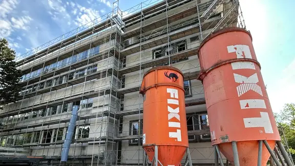 Deux silos Fixit orange au premier plan devant un bâtiment à plusieurs étages entouré d'échafaudages à Zurich.